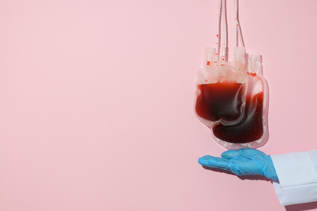 Foto sacchetti con sangue donato e mano dei medici su sfondo rosa spazio per il testo