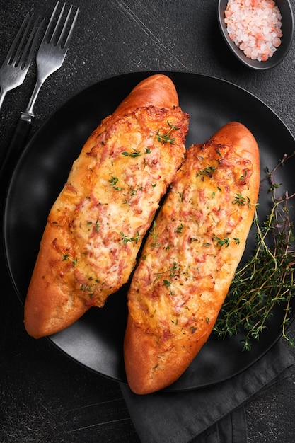 Baguette boats Hot baked sandwich on baguette bread with ham bacon vegetables and cheese on parchment and black dark concrete background Top view Copy space