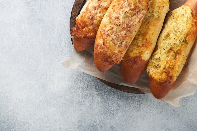 Baguette boats Hot baked sandwich on baguette bread with ham bacon vegetables and cheese on parchment and wooden stand on gray concrete background Top view Copy space