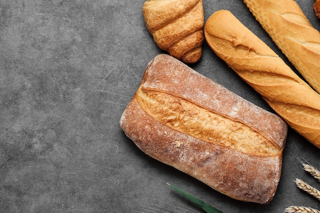 Baguette croissant and ciabatta Fresh baked wheat bread lies on a gray table Various types of freshly baked bread Bakery top view local bakery concept