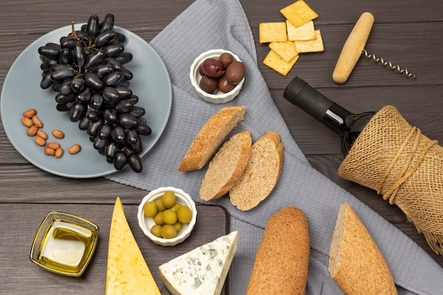 Baguette and olives in bowls on a gray napkin Black grapes on a gray plate