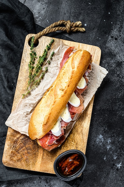Baguette sandwich with prosciutto ham, Camembert cheese on a cutting Board.