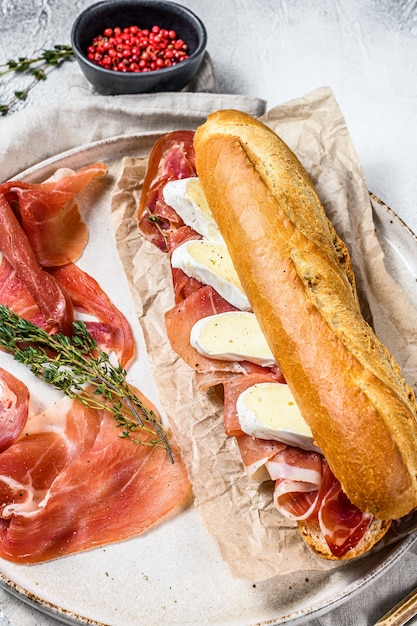 Baguette sandwich with prosciutto ham, Camembert cheese on a plate. Gray background, top view.