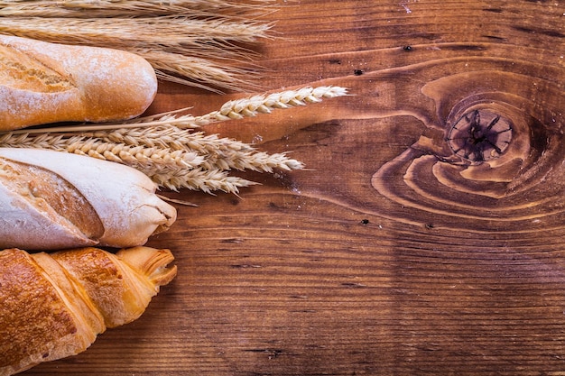 Baguettes and croissant with wheat ears on old wooden board