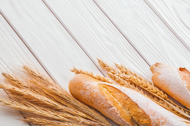 Baguettes and ears of wheat on old white wooden boards with copyspace