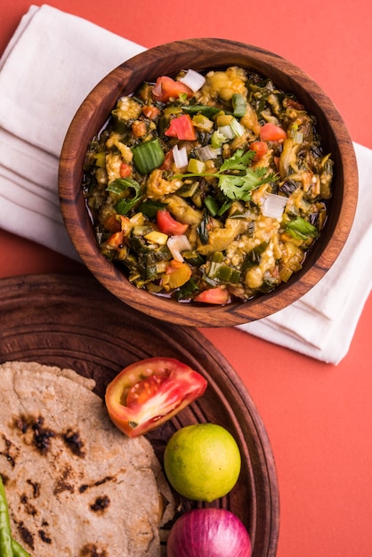 Photo baigan /baingan bharta - mashed roasted eggplant cooked with spices & vegetables. served with jowar flour flat bread known as bhakar/bhakri. served over colourful or wooden background