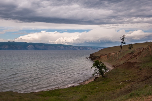 Baikal oever van het meer met bergen op de achtergrond en prachtige wolken. Bomen aan de oever van het meer. Meer met golven.