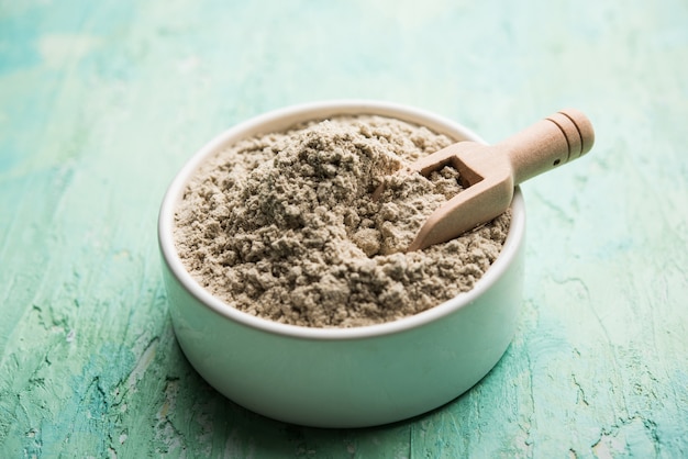 Bajra atta or flour of pearl millet powder served in a bowl with small wooden scoop, selective focus