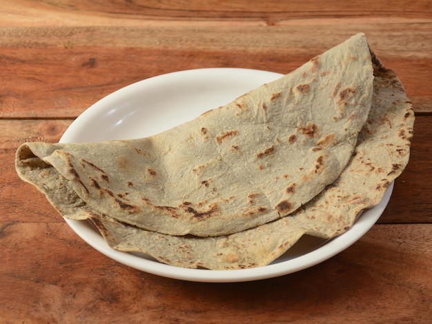 写真 bajra roti または bajra bhakri は伝統的なインドの平らなパンで、素朴な木製のテーブルのセレクティブ フォーカスで提供される bajra または黒真珠キビ粉で作られました。