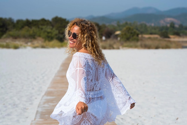 Bak view of adult woman with white beachwear walking happy and free at the beach on white sand in tropical summer holiday vacation destination Cheerful female people in outdoor leisure activity