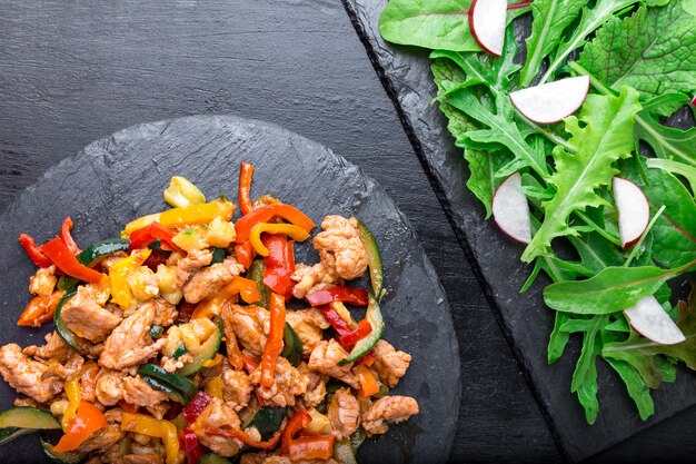 Bak vlees met groenten in de buurt van salade met rucola en radijs op stenen leisteen platen. Avondeten. Heerlijke gezonde lunch. Bovenaanzicht