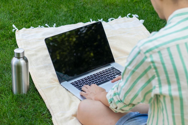 Bakc-weergave van onherkenbare jonge online met behulp van een laptop op een handdoek en een fles water aan de zijkant