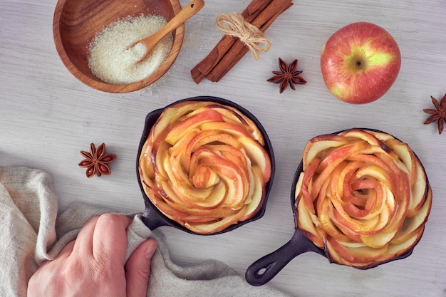 Baked apple roses in iron skillets, top view on wooden board