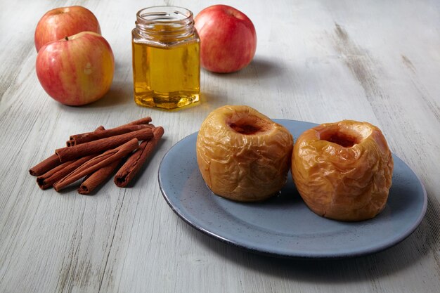 Baked apples on a blue plate with honey, cinnamon and ginger on a light wooden table. Home recipe.