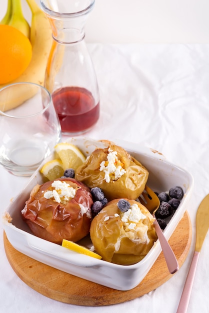 Baked apples with blueberries and cottage cheese in bowl with cutlery on white table