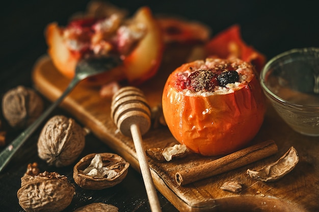 Запеченные яблоки с творогом с ягодами и орехами, посыпанные медом и посыпанные корицей. на деревянной поверхности в деревенском стиле