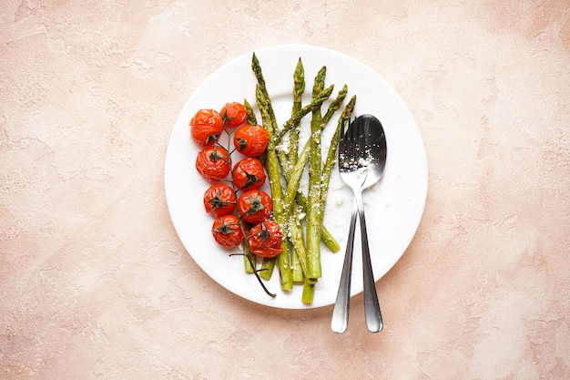 Baked asparagus and cherry tomatoes in a plate on a beige background. Top view.