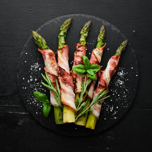 Baked asparagus with bacon and spices on a black stone plate Top view Free space for your text