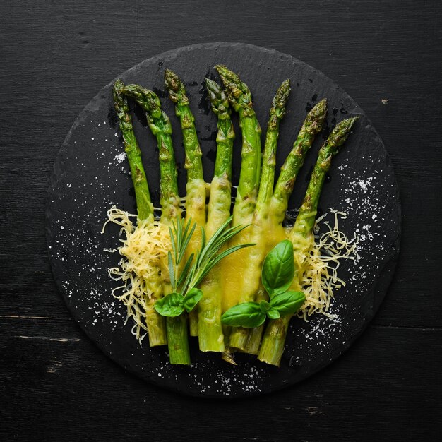 Baked asparagus with cheese and basil on a black stone plate Top view Free space for your text