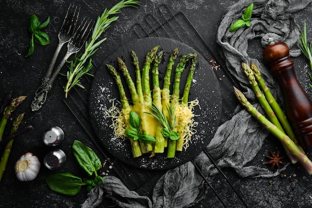 Baked asparagus with cheese and basil on a black stone plate Top view Free space for your text