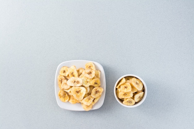 Baked banana chips in a white bowl and saucer on the table