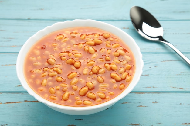 Photo baked beans in tomato sauce in a white ceramic bowl on blue background