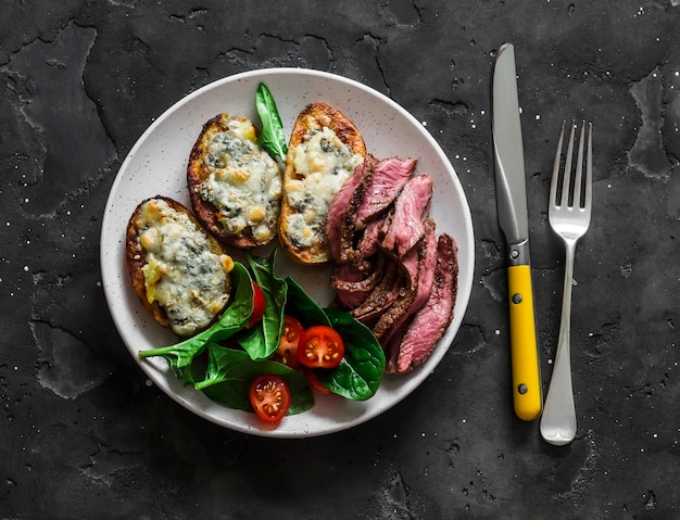 Baked blue cheese potatoes beef steak and vegetable salad on a dark background top view