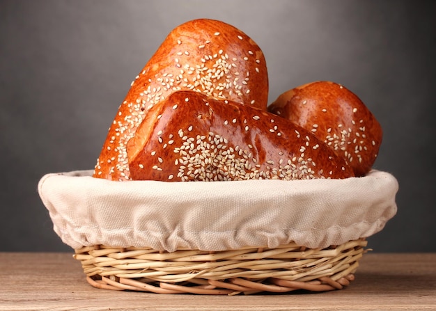 Baked bread in basket on wooden table on grey background