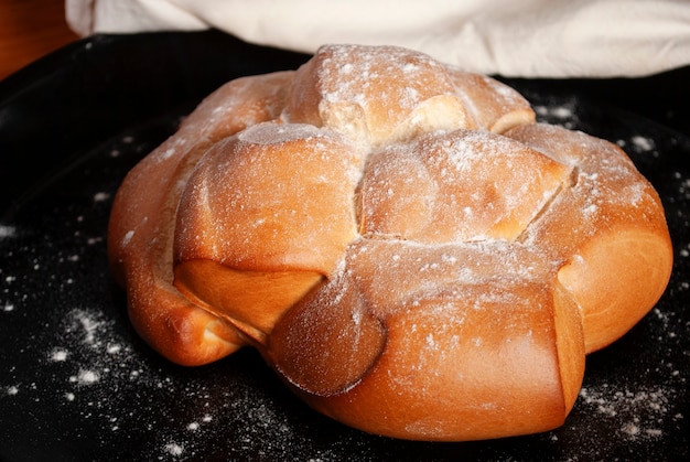 A baked bread on a black baking sheet sprinkled with flour.
