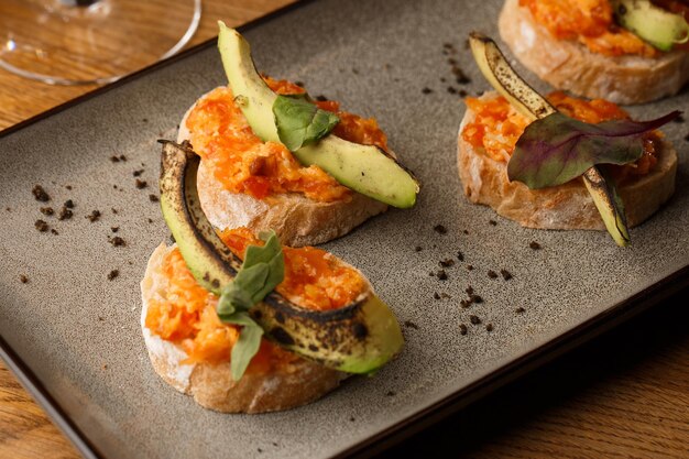 Foto bruschetta al forno con formaggio salmone pomodori secchi e avocado in lamiera grigia su sfondo luminoso