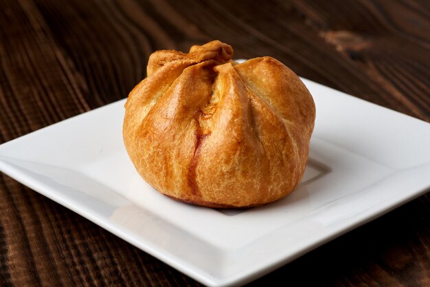 Baked bun on a white plate on a wooden table