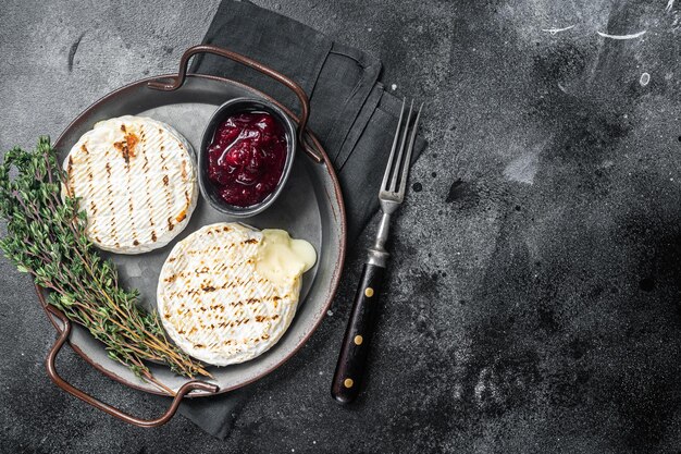 Baked Camembert cheese on a steel tray with cranberry sauce and thyme Black background Top view Copy space