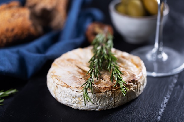 Baked camembert cheese with rosemary, olives and bread, close up