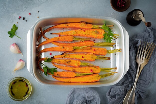 Baked carrots with spices, garlic and olive oil in a simple aluminum form on a gray concrete.  