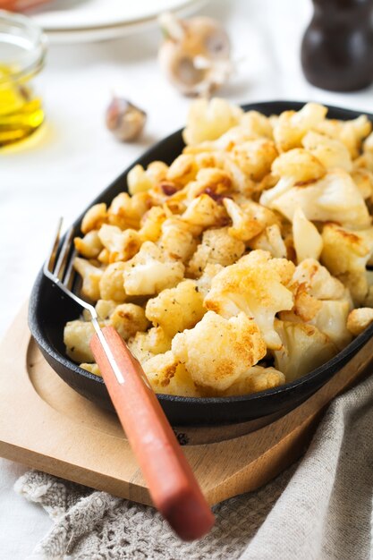 Baked cauliflower with spices and garlic in a cast-iron frying pan on a light surface. Selective focus.