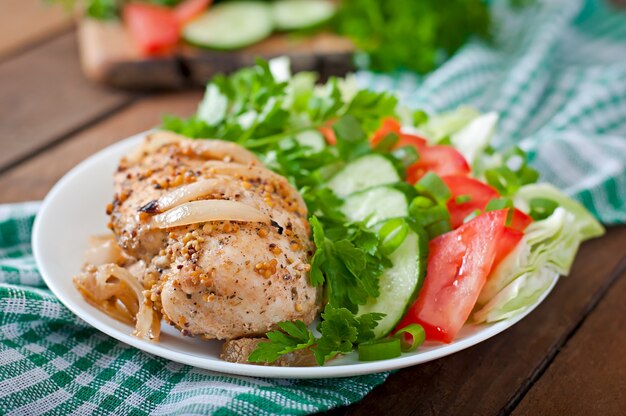 Baked chicken breast and fresh vegetables on plate on a wooden table