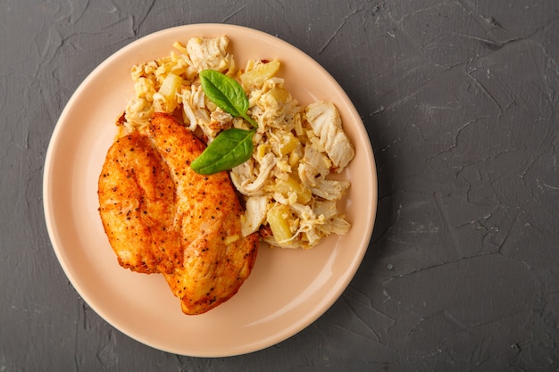 Baked chicken breast on a plate with pineapple salad on a table on a concrete background. Horizontal photo