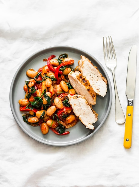 Baked chicken breast with beans spinach paprika tomato sauce on a light background top view Healthy balanced food concept