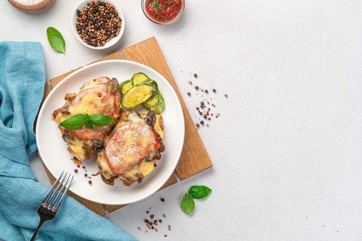 Запеченная куриная грудка с грибами, овощами и сыром на светлом фоне. Вид сверху, копия пространства.