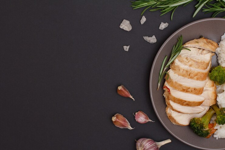 Photo baked chicken breasts or fillet on plate with rosemary and garlic on black background. top view.