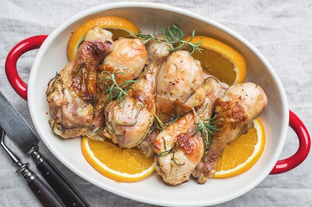 Baked chicken drumstick in a dish with orange and rosemary, top view