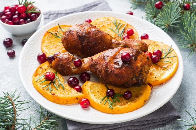 Baked chicken drumstick with oranges and cranberries in a plate. Christmas food Table with decorations.