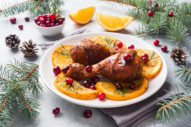 Baked chicken drumstick with oranges and cranberries in a plate light grey background. 