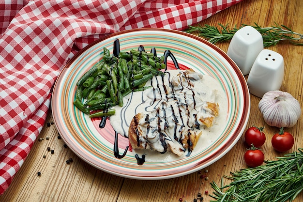 Baked chicken fillet with cream sauce and asparagus side dishes in a ceramic plate on wood. Close up