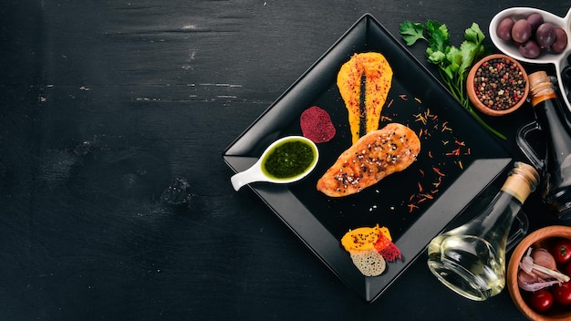 Baked chicken fillet with sauce on a black plate On a wooden background Free space for text Top view