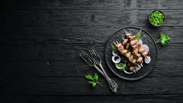 Cuore di pollo al forno su spiedini in un piatto nero carne di pollo vista dall'alto spazio libero per il testo