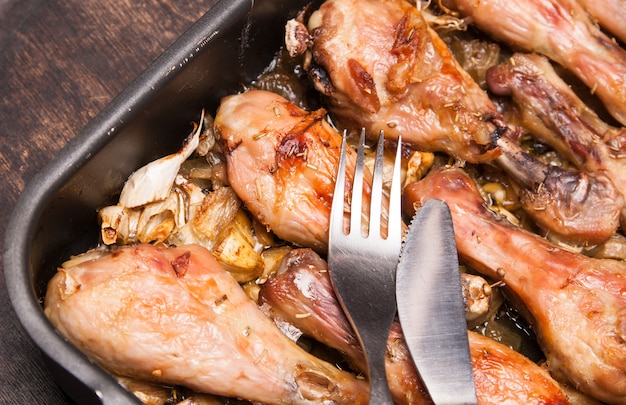 Baked chicken legs in tray on black wooden