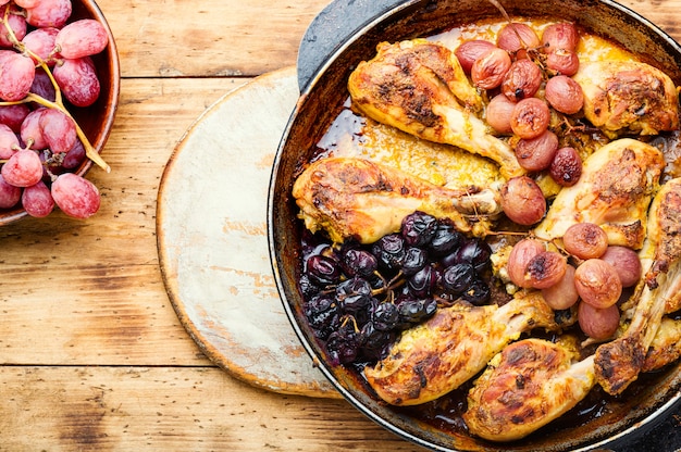 Baked chicken legs with grapes in pan on wooden background