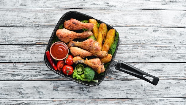 Baked Chicken legs with potatoes and vegetables on a white wooden background Meat Top view Free copy space