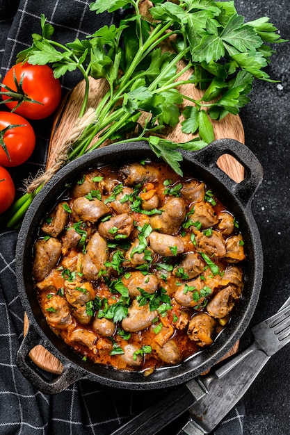 Baked chicken liver hearts in the cast iron pan.  Black background. Top view